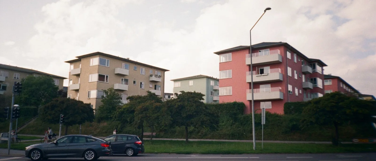 Flerfamiljshus längs en gata med bilar i förgrunden.