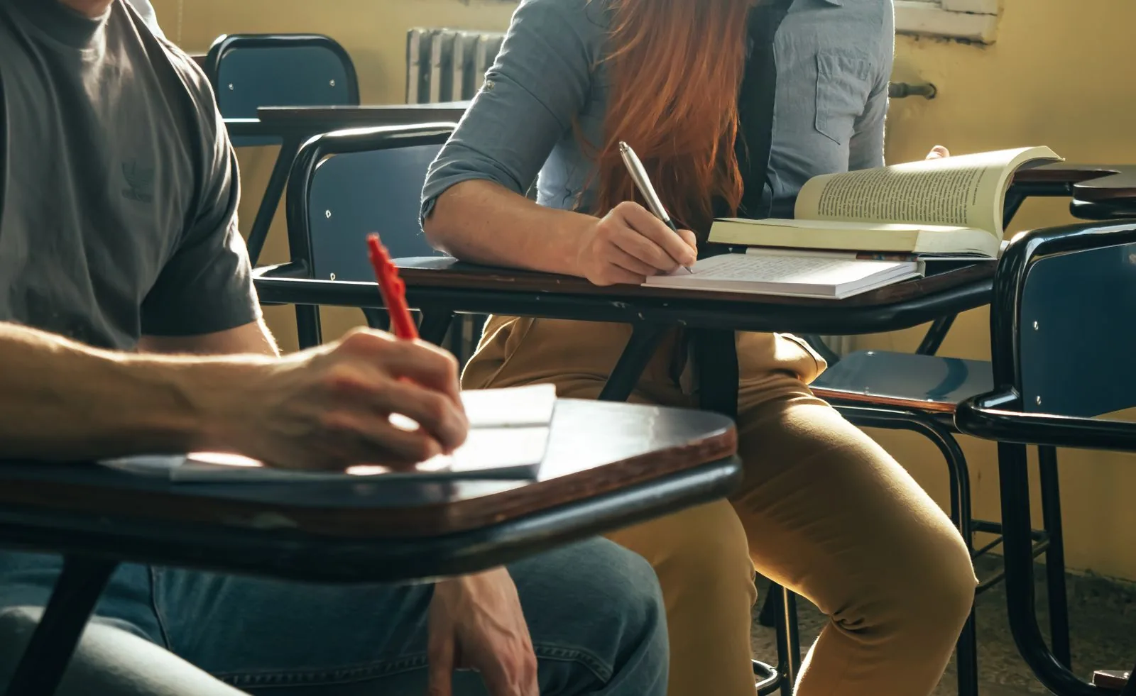 Två personer antecknar för hand vid skolbänkar i ett klassrum.