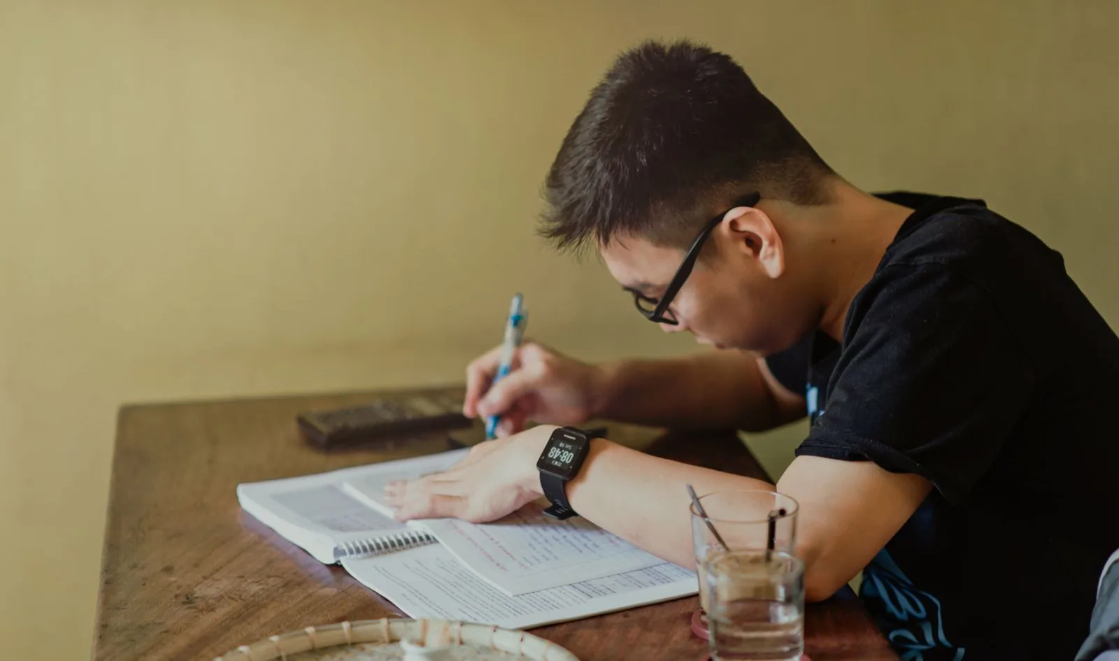 Person sitter vid ett bord och skriver i ett block bredvid en uppslagen bok.
